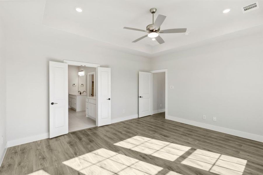 Unfurnished bedroom with connected bathroom, wood-type flooring, and ceiling fan