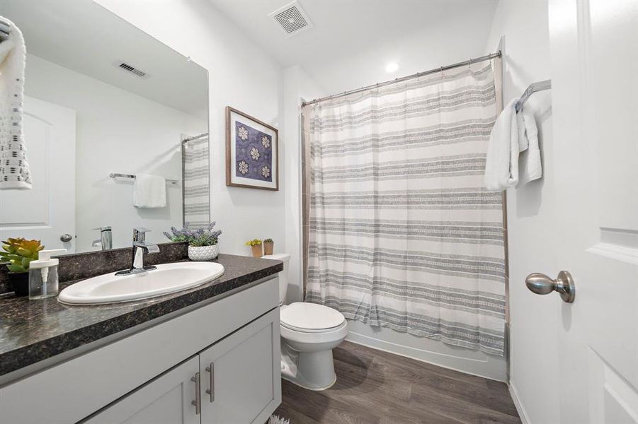 The secondary bathroom featuring a single vanity with ample storage, a granite countertop with an undermount sink, a large mirror, and a tile tub/shower combo.