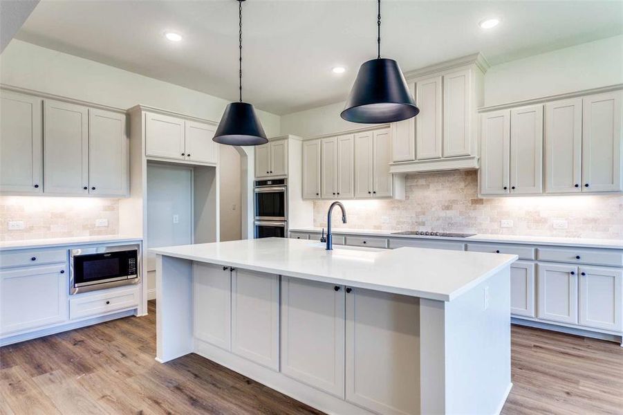 Kitchen with sink, appliances with stainless steel finishes, hanging light fixtures, an island with sink, and light hardwood / wood-style flooring