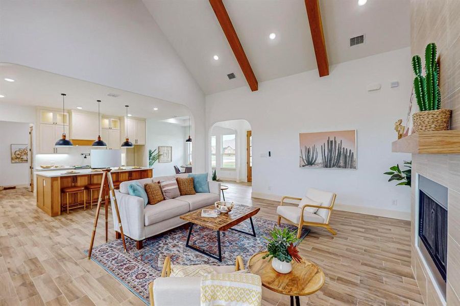 Living room with light hardwood / wood-style floors, high vaulted ceiling, beam ceiling, and a fireplace