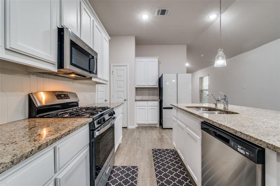 Kitchen featuring white cabinetry, sink, pendant lighting, light hardwood / wood-style floors, and stainless steel appliances