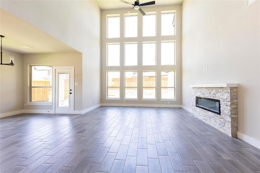 Unfurnished living room featuring dark hardwood / wood-style floors, a stone fireplace, a high ceiling, and ceiling fan