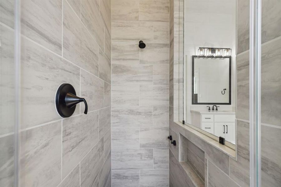 Matching tile work in the shower provides consistency in design. Early mornings are made brighter and warmer in the spacious shower featuring recessed lighting and a built-in shelf for self-care items!