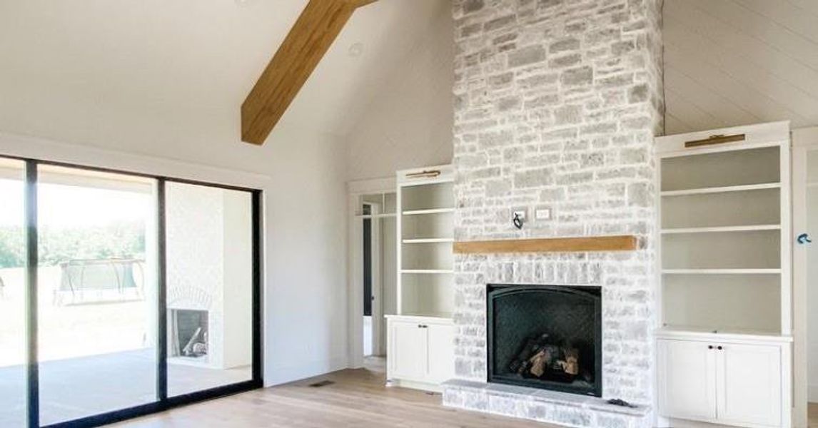 Unfurnished living room featuring lofted ceiling with beams, light hardwood / wood-style floors, and a stone fireplace