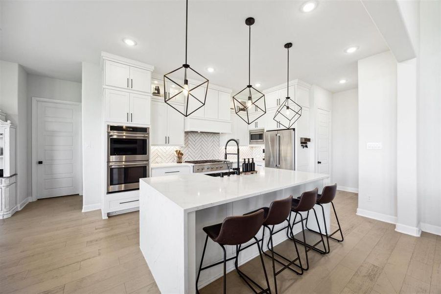 Modern kitchen with white cabinetry, stainless steel appliances, a large island with seating, and stylish pendant lighting.