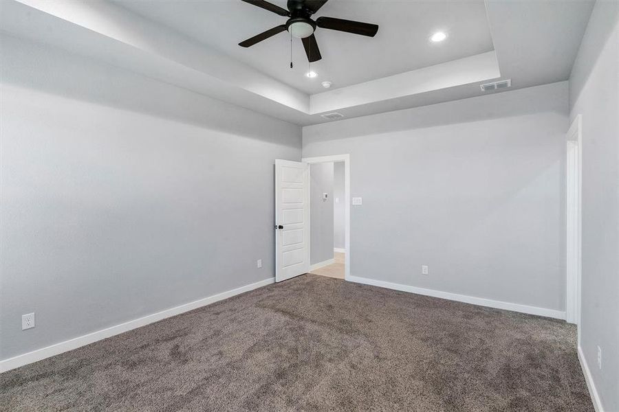 Carpeted spare room featuring a tray ceiling and ceiling fan