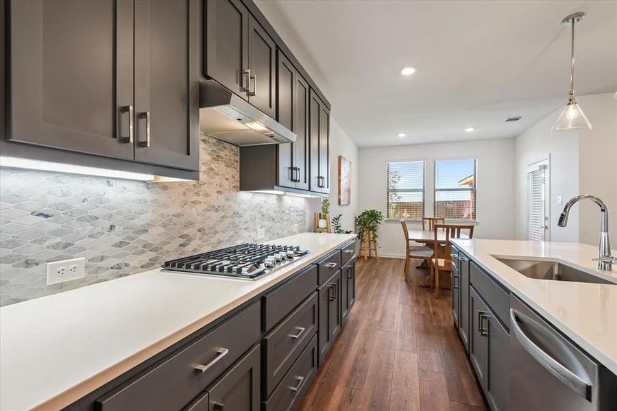 Kitchen with tasteful backsplash, sink, stainless steel appliances, decorative light fixtures, and dark hardwood / wood-style floors