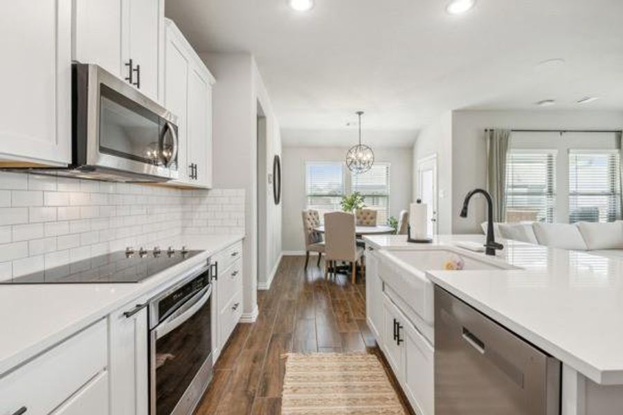 Kitchen with tasteful backsplash, dark wood-type flooring, a kitchen island with sink, appliances with stainless steel finishes, and pendant lighting