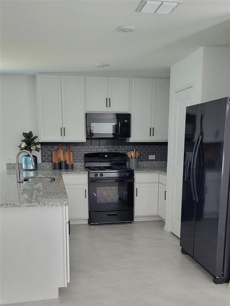 Kitchen with white cabinetry, black appliances, sink, and light tile flooring