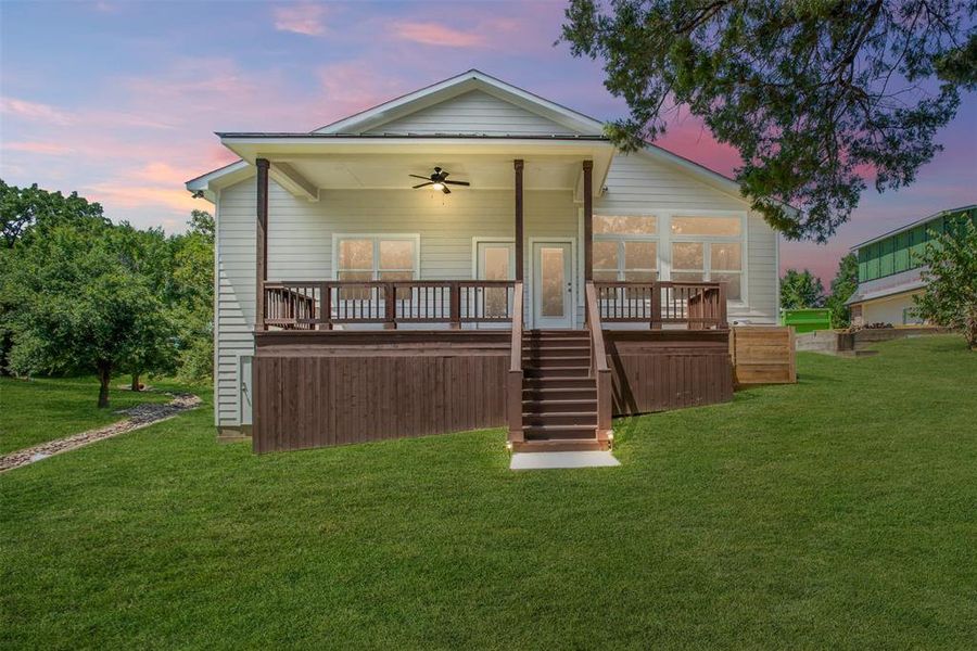 Back house at dusk with ceiling fan, a wooden deck, and a lawn