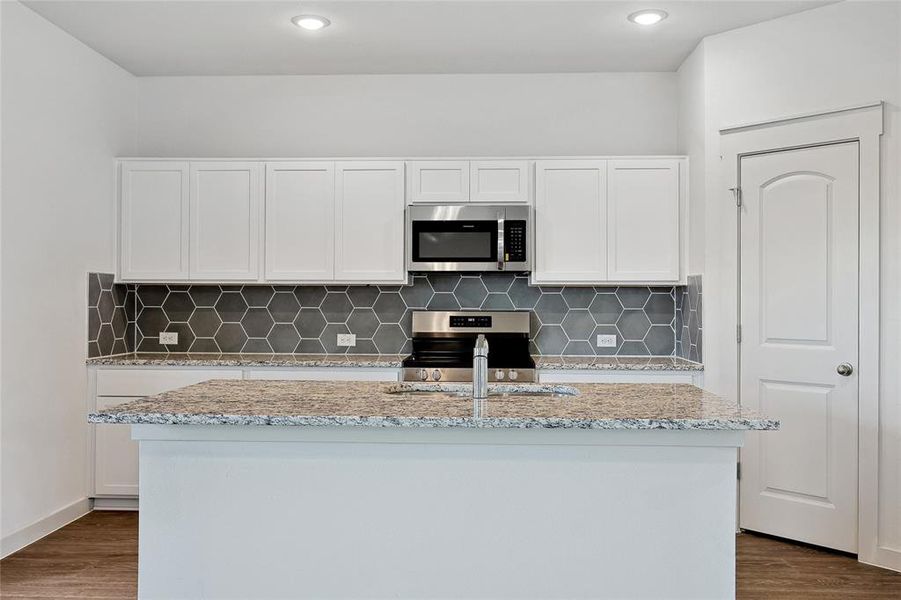 Kitchen with appliances with stainless steel finishes, a kitchen island with sink, dark wood-type flooring, and white cabinets