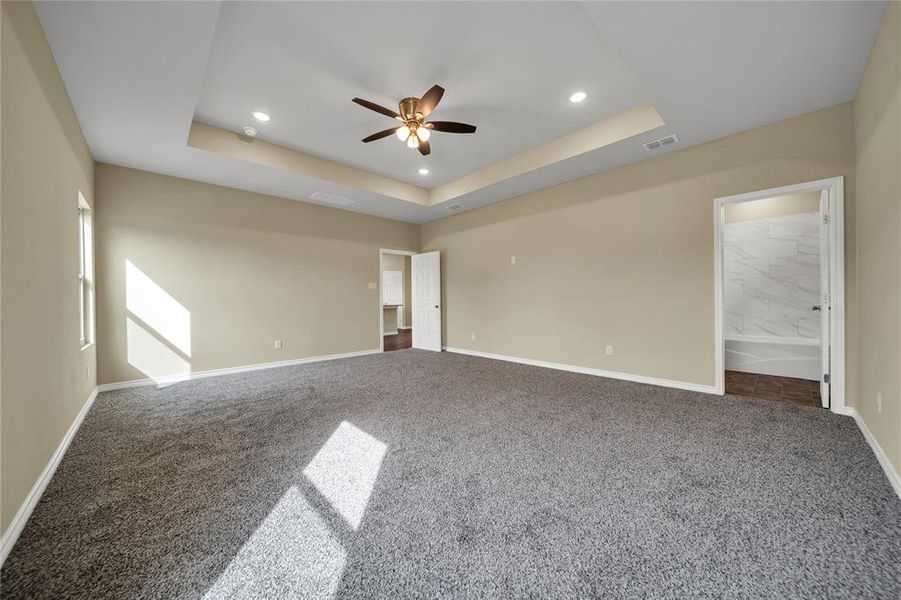 Carpeted spare room featuring ceiling fan and a raised ceiling