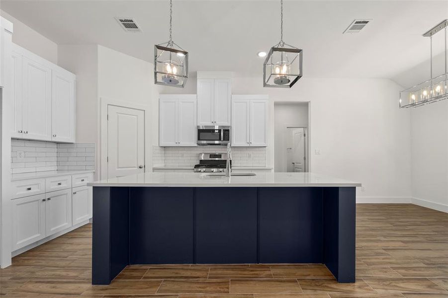 Kitchen featuring tasteful backsplash, stainless steel appliances, pendant lighting, an island with sink, and hardwood / wood-style flooring