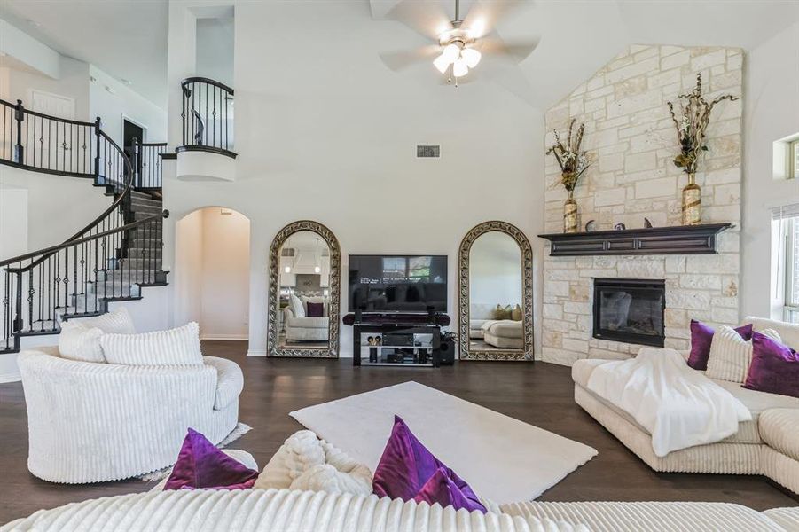 Living room with a stone fireplace, dark hardwood / wood-style floors, ceiling fan, and high vaulted ceiling