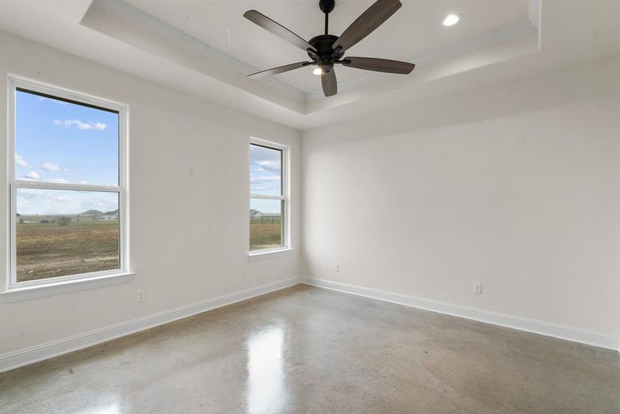 Empty room with ceiling fan, concrete floors, a raised ceiling, and ornamental molding