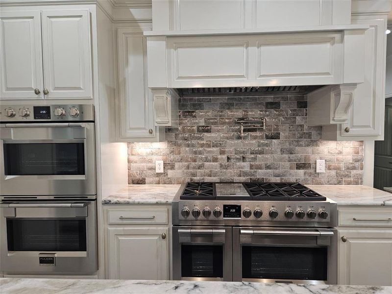 Kitchen with decorative backsplash, white cabinets, appliances with stainless steel finishes, and light stone countertops