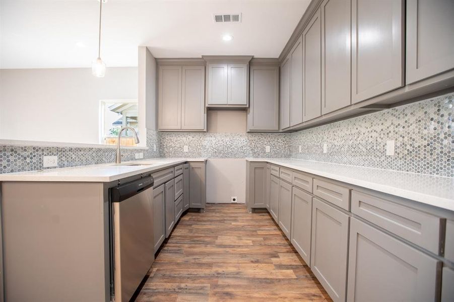 Kitchen with stainless steel dishwasher, hardwood / wood-style floors, and backsplash