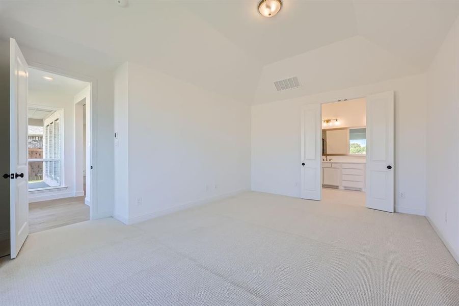 Unfurnished bedroom featuring lofted ceiling, ensuite bath, and light colored carpet