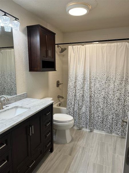 Full bathroom with vanity, toilet, a textured ceiling, and shower / tub combo