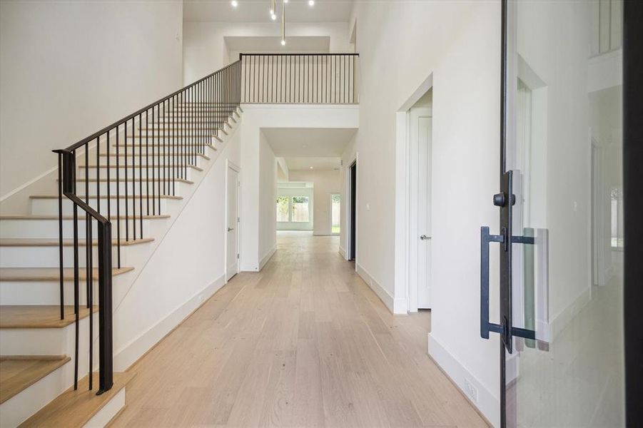 A towering foyer features a wood staircase with black metal balusters, White Oak hardwood floor, quartzite countertops and fresh white walls throughout. There’s a clear view to the second floor landing and light-filled great room.