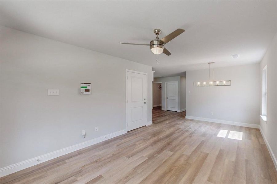 Empty room with light wood-type flooring and ceiling fan with notable chandelier