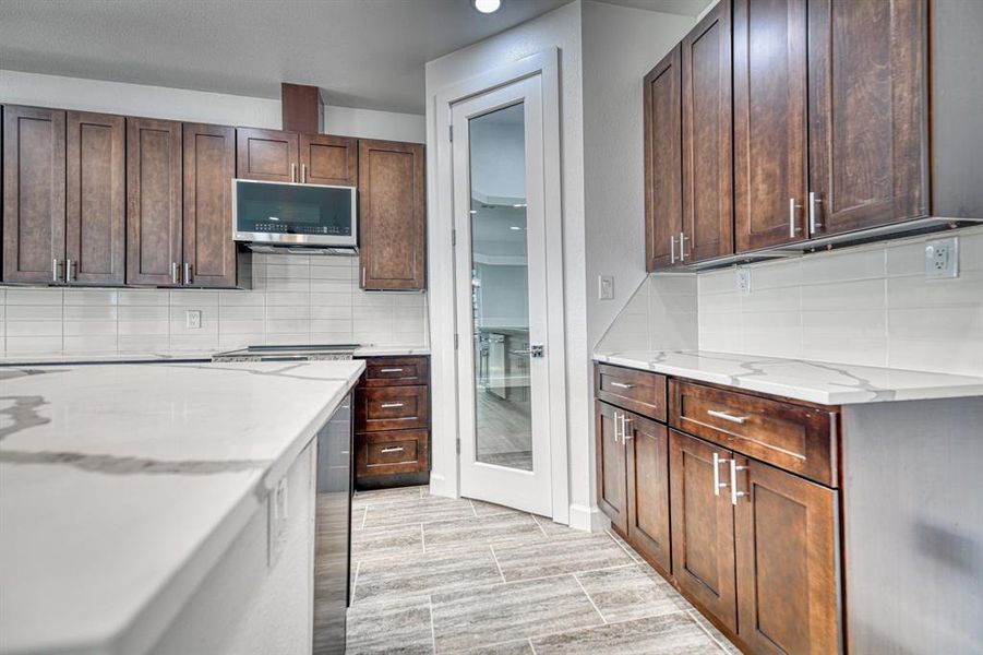 Kitchen with dark brown cabinetry, light stone counters, and light wood-type flooring