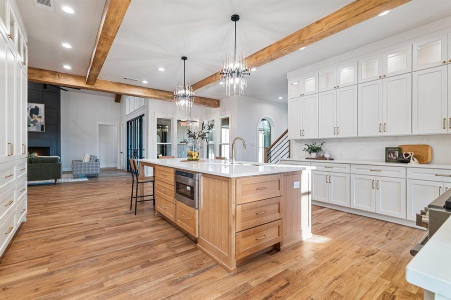 Kitchen featuring light hardwood / wood-style floors, white cabinetry, beamed ceiling, a kitchen island with sink, and pendant lighting