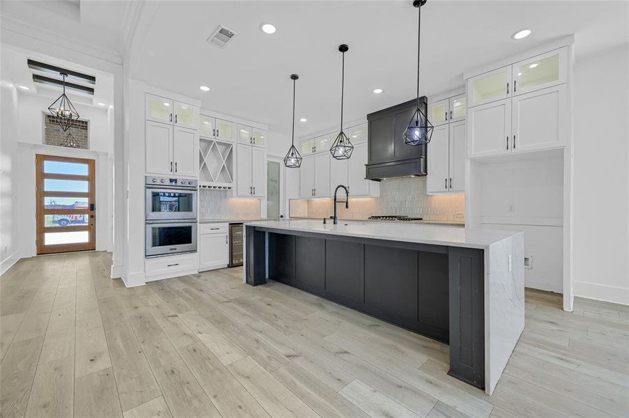 Kitchen with appliances with stainless steel finishes, white cabinets, a center island with sink, light hardwood / wood-style floors, and decorative backsplash