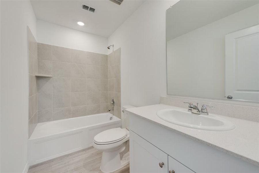 Full bathroom featuring hardwood / wood-style floors, vanity, tiled shower / bath combo, and toilet