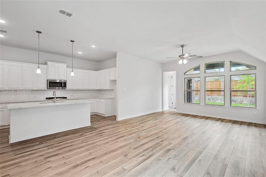 Kitchen featuring white cabinetry, light hardwood / wood-style floors, lofted ceiling, and a center island with sink