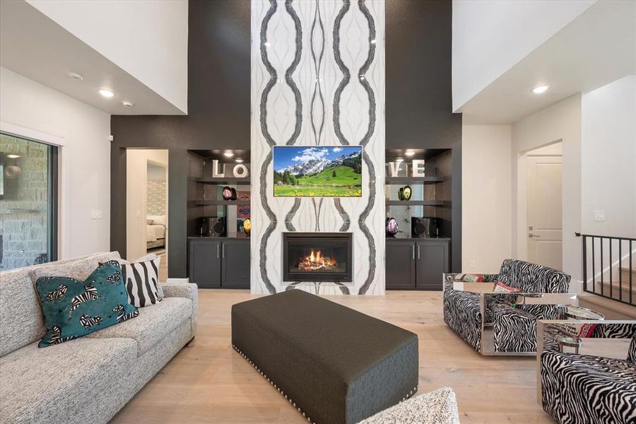 Living room featuring a towering ceiling, a high end fireplace, and light hardwood / wood-style flooring