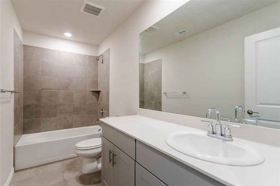 Full bathroom upstairs featuring tile patterned floors, vanity, tiled shower / bath combo, and toilet