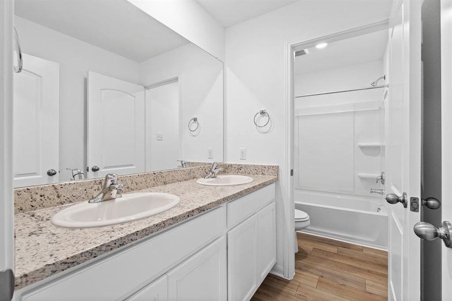 Secondary bathroom includes double vanities, granite counters, designer white cabinetry and luxury vinyl plank flooring.