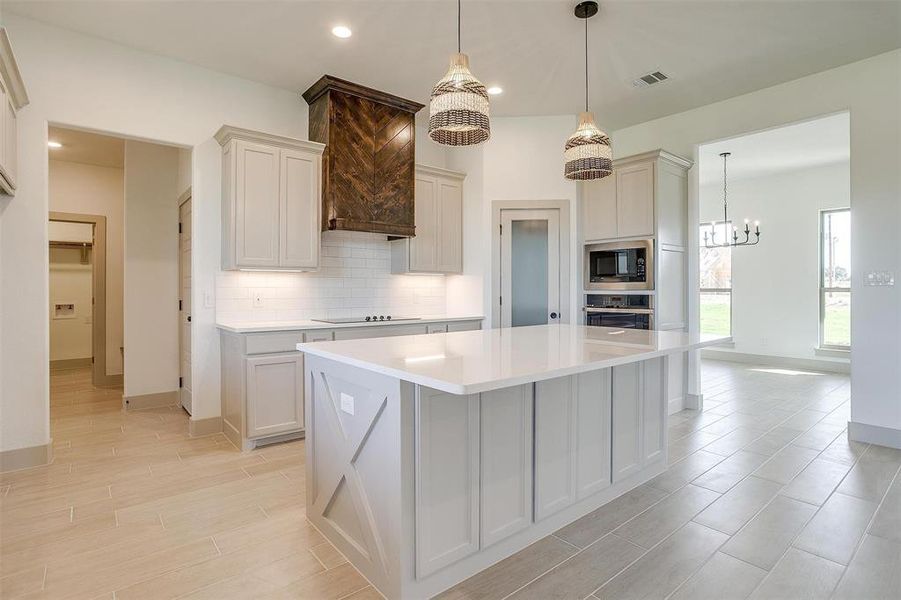 Kitchen featuring built in microwave, a large island, hanging light fixtures, and stainless steel oven