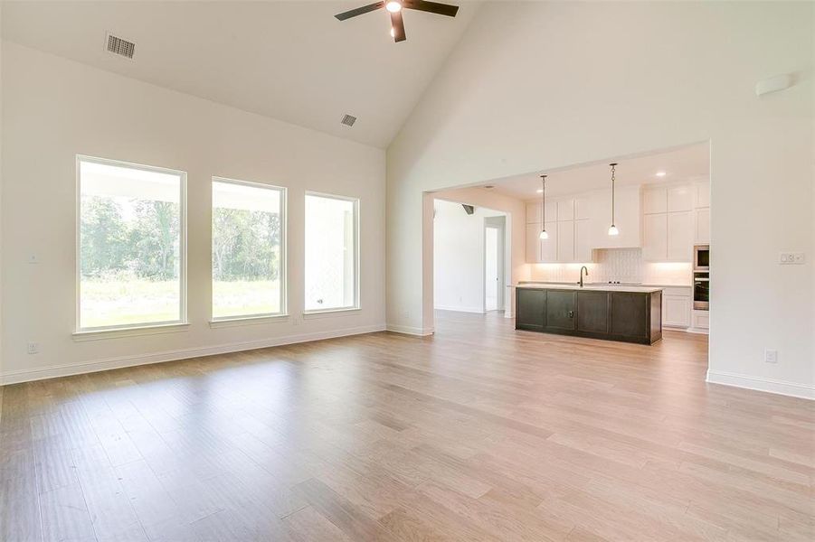 Unfurnished living room featuring light hardwood / wood-style flooring, high vaulted ceiling, ceiling fan, and plenty of natural light