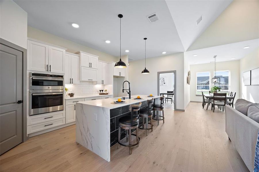 Kitchen featuring a breakfast bar, white cabinetry, a kitchen island with sink, light wood-type flooring, and stainless steel double oven