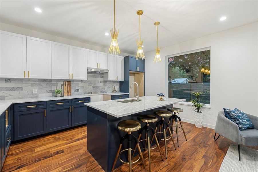Kitchen featuring blue cabinets, hanging light fixtures, dark hardwood / wood-style flooring, sink, and backsplash