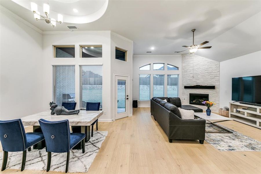 Living room featuring a high ceiling, a stone fireplace, crown molding, light wood-type flooring, and ceiling fan with notable chandelier