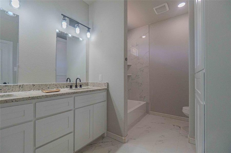 Full bathroom featuring tile floors, tiled shower / bath, double sink vanity, and toilet