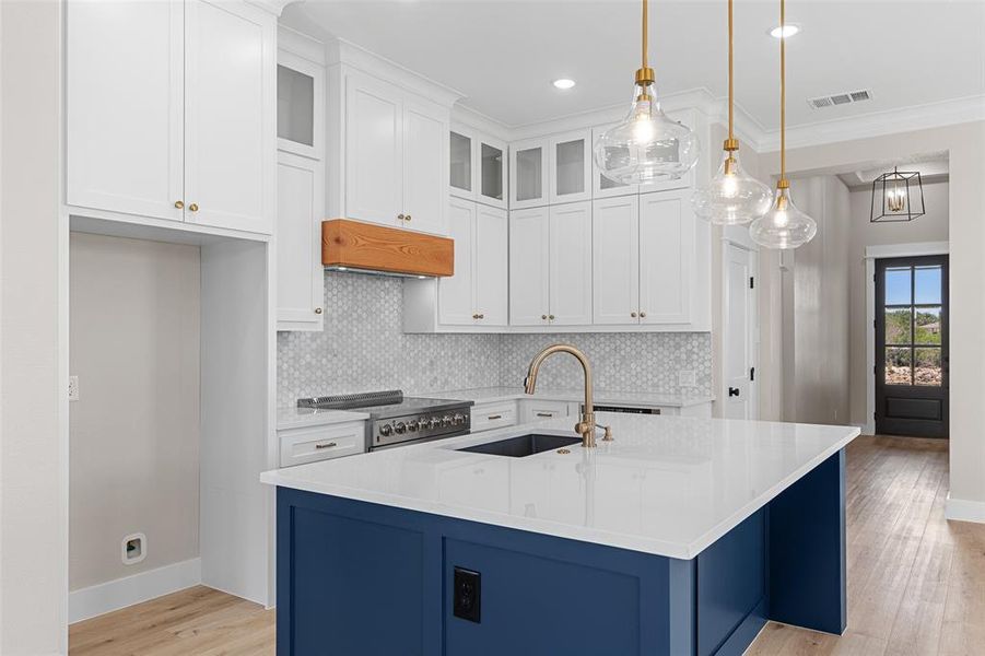 Kitchen featuring white cabinets, pendant lighting, crown molding, a center island with sink, and sink