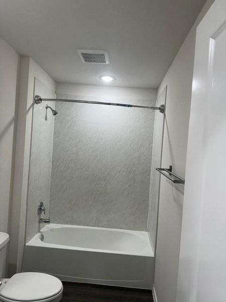 Bathroom featuring hardwood / wood-style floors, tiled shower / bath, and toilet