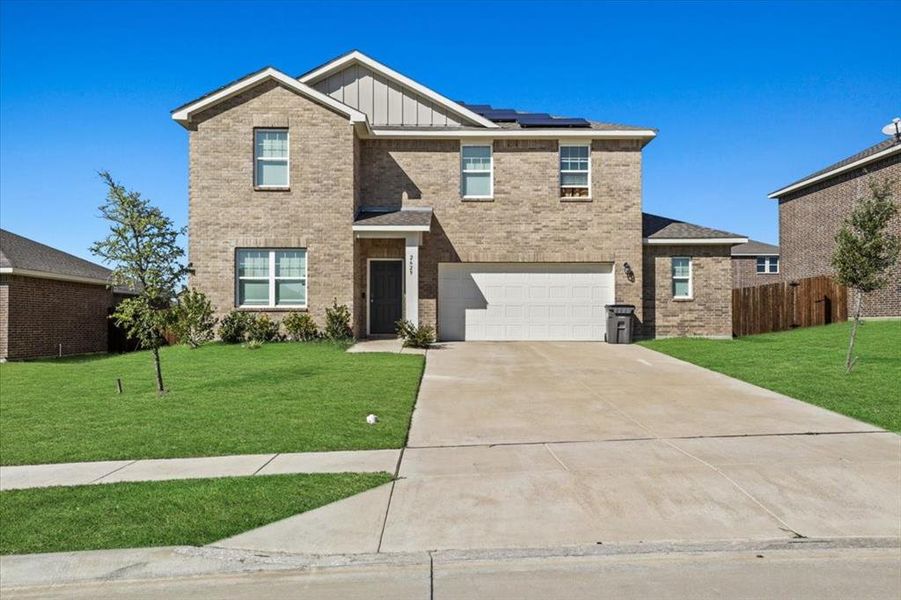 View of front of home with a front yard, solar panels, and a garage