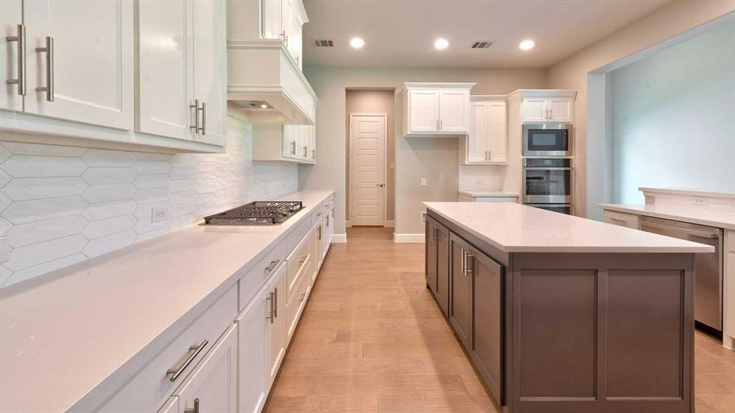 Kitchen with stainless steel appliances, white cabinets, backsplash, light wood-type flooring, and a center island