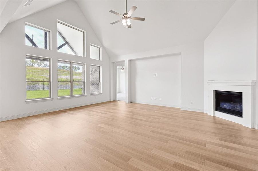 Unfurnished living room with high vaulted ceiling, ceiling fan, and light wood-type flooring