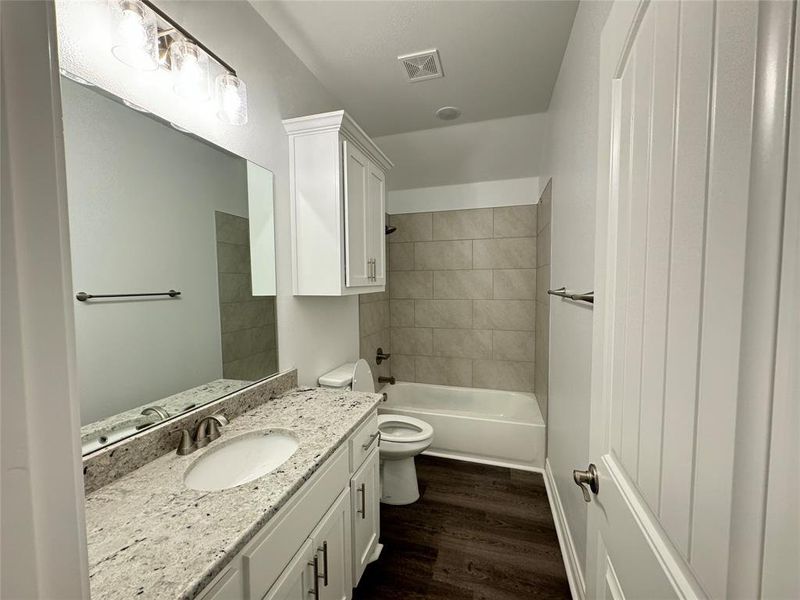Full bathroom with vanity, tiled shower / bath combo, wood-type flooring, and toilet