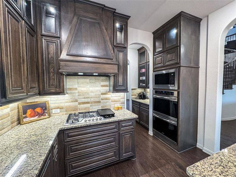 Kitchen with decorative backsplash, custom range hood, stainless steel appliances, and dark hardwood / wood-style flooring