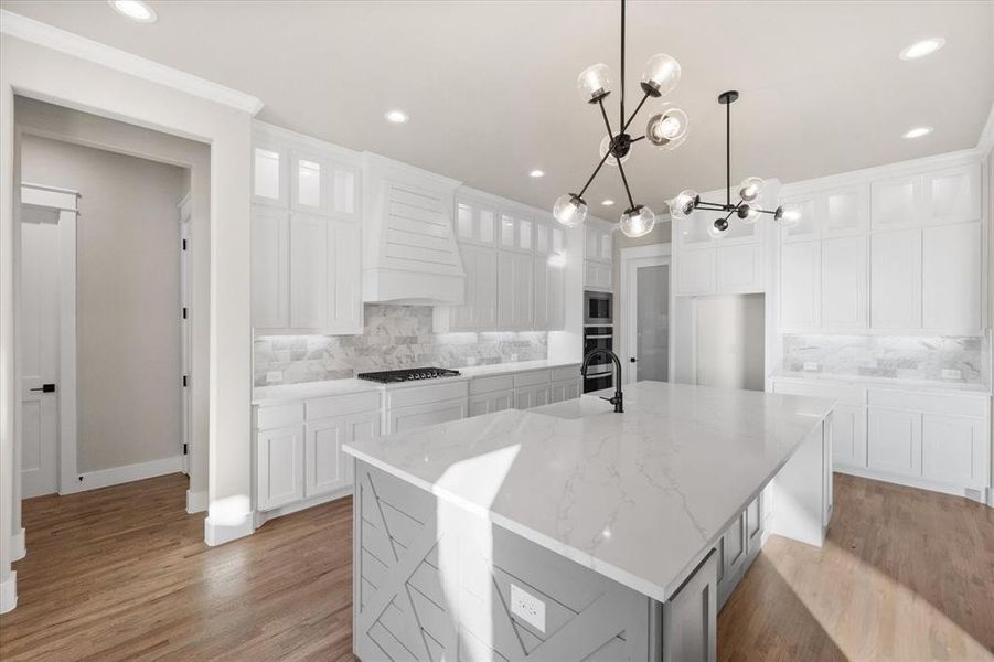 Kitchen with a spacious island, white cabinets, light hardwood / wood-style floors, and tasteful backsplash