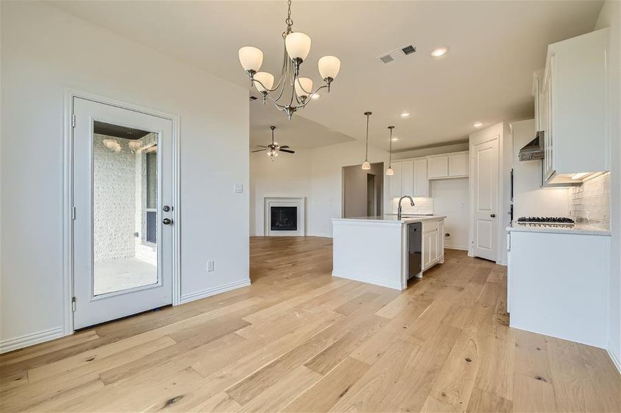 Kitchen featuring light hardwood / wood-style floors, pendant lighting, backsplash, white cabinets, and a kitchen island with sink