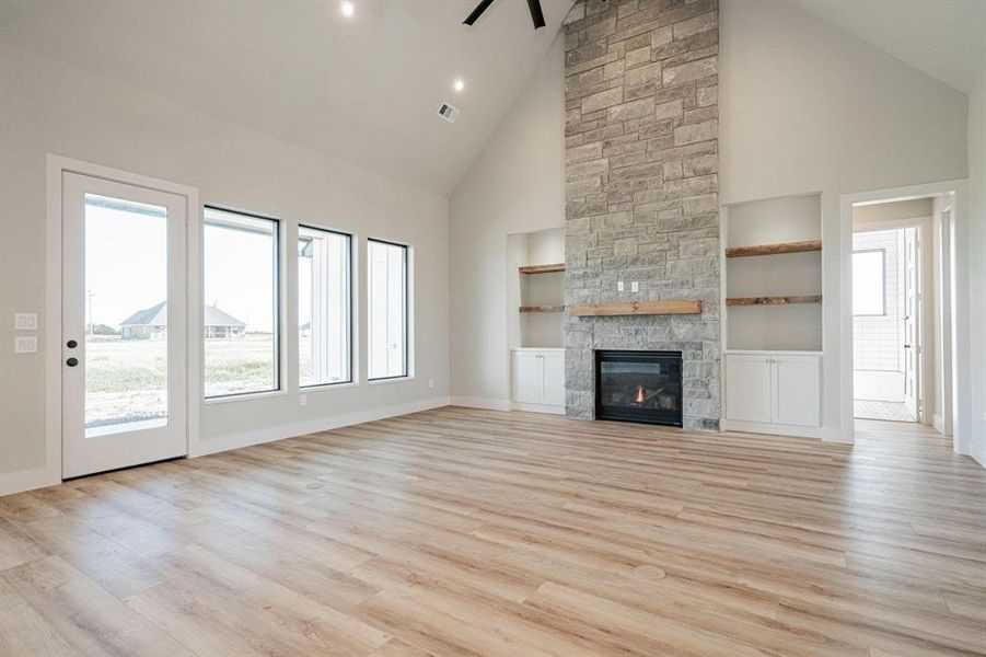 Example of living room featuring light hardwood / wood-style floors, high vaulted ceiling, plenty of natural light, and a stone fireplace