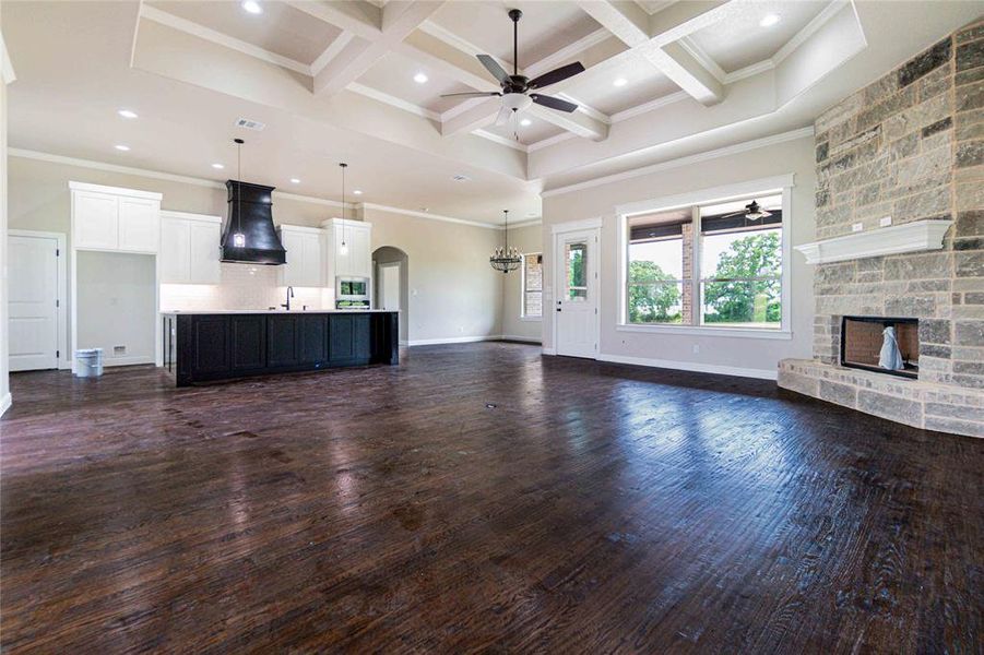 Unfurnished living room featuring a stone fireplace, dark wood-type flooring, ceiling fan, and coffered ceiling